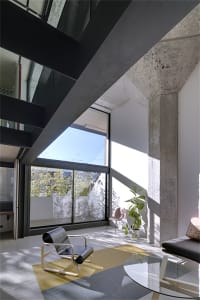 Modern industrial living room featuring concrete walls, glass windows, and minimalist furniture.