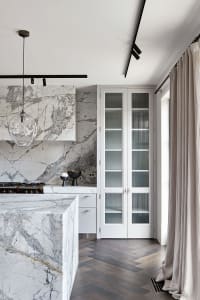 A modern kitchen with marble countertops and flooring, featuring white cabinetry and a minimalist design.