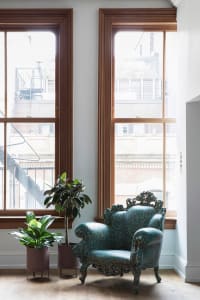 A modern, blue, scale-shaped armchair in a living space with a large window and plants.