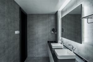 A modern bathroom with black and gray ceramic tiles, a white countertop sink, and a large rectangular mirror.
