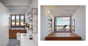 Modern home office featuring a desk, bookshelf, and floor-to-ceiling window overlooking a balcony and landscape.