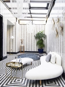 A modern living room with a white curvilinear sofa, a round metal table, a decorative floor lamp, and a large potted plant.