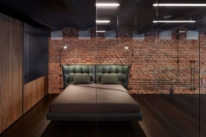 Modern bedroom with industrial design featuring a bed made of leather and metal, with a brick wall and wooden floor.