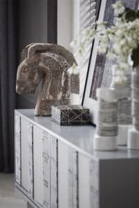 A modern decorative wooden horse sculpture placed on a sleek, white cabinet.