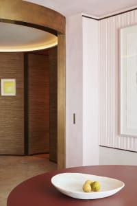 A modern interior design scene featuring a white table with a bowl of fruit, set against a pink textured wall and a wooden do