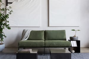 A modern living room featuring a green upholstered sofa with minimalist design elements, black metal coffee tables, and a whi