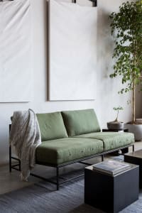 A modern industrial-style sofa with green cushions and metal frame in a living room setting.