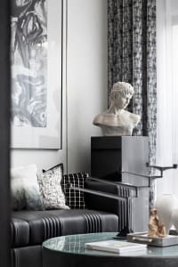 A modern living room featuring a metal and leather sofa with a black and white checkered cushion, a decorative bust, and a gl