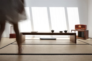 A modern living room features wood furniture and a concrete floor with large windows allowing natural light to flood the spac