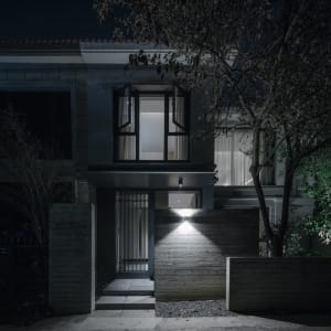 A modern house facade made of concrete with lights illuminating the entrance.