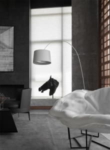 A modern living room with a concrete floor, white armchair, black floor lamp, and minimalistic decor.