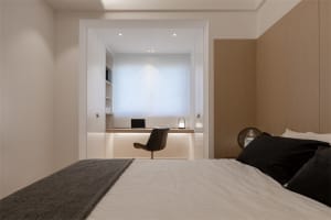 A minimalist bedroom featuring a wooden-panelled headboard and a sleek, modern desk area.