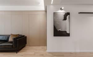Modern minimalist living room with black leather sofa, wooden flooring, and abstract black-and-white artwork.