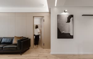 A modern living room with a black leather sofa, wooden flooring, and minimalist decor.