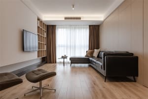 Modern living room featuring a black leather sectional sofa, wooden flooring, and a flat-screen TV mounted on the wall.