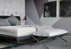A modern minimalist bedroom featuring a black leather bed with grey pillows, a white blanket, and a grey upholstered bench.