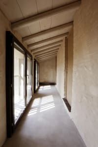 A narrow corridor with concrete walls, a brick ceiling, and sunlight streaming through a glass door.