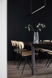 A minimalist dining room featuring wooden furniture and a dark wall.