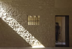 A modern interior design featuring a stone wall with light penetrating through a small window, creating dramatic shadows and 