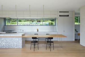 Modern kitchen with minimalist design, marble countertops, stainless steel appliances, and large windows overlooking greenery