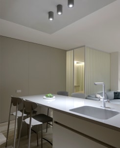 A minimalist residential kitchen featuring a white marble countertop with a built-in sink and three stools.