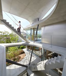 Person descending open staircase with curving concrete railings and glass balustrade, modern residential architecture, concre