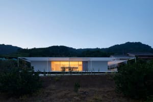 Modern minimalist concrete house at dusk with illuminated interior.