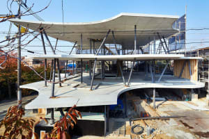 A modern construction site featuring concrete and steel structures under a clear blue sky, with trees and electrical poles in