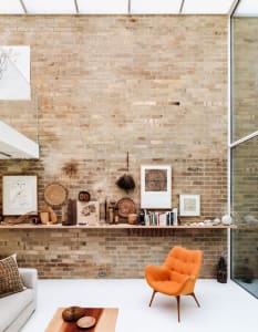 A modern living room featuring a brick wall, an orange armchair, a wooden coffee table, and various decorative items on a low