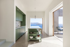 Modern minimalist kitchen with green wooden furniture and a concrete floor, featuring a view of the sea through large windows
