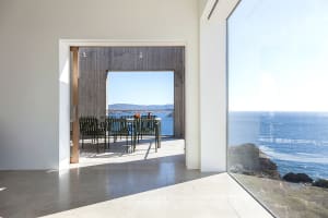 A modern, minimalist residential dining area with concrete walls and flooring, featuring a table and chairs overlooking the o