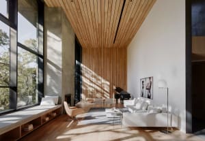 A modern living room with a white couch, wooden floor, concrete wall, and large windows showcasing a serene outdoor view.