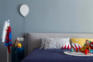 A modern bedroom with a gray upholstered headboard, blue bedding, and colorful plush toys.