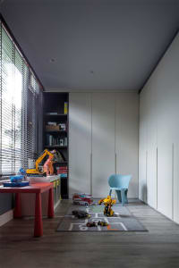 A minimalist playroom with wall storage, featuring a red table, wooden floor, and toys on a hopscotch mat.