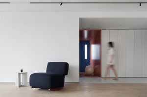 A modern living room with minimalist furnishings, including a navy blue upholstered chair on red rocking legs, a white side t