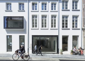 Modern street view featuring a coffee shop with glass and concrete facade, people walking by, and a cyclist.