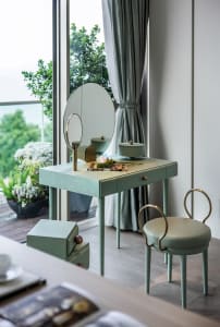 A modern vanity with wooden legs, a circular mirror, and a green cushioned stool.