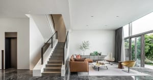 A modern minimalist living room with a brown leather sofa, white coffee table, and large windows.