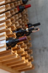 A modern wooden wine rack holding several bottles of wine.