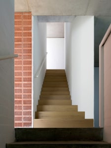 Modern minimalist staircase with concrete steps, white walls, and red brick wall.