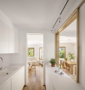 A minimalist residential interior with white walls, flooring, and cabinets, featuring a kitchen counter, a dining area, and a