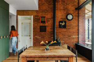A modern dining room with a rustic brick wall, a wooden table, and a flower arrangement in the vase.