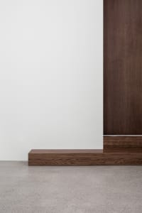A modern interior featuring a wooden floor, contrasting with a white wall and a wooden vertical panel.