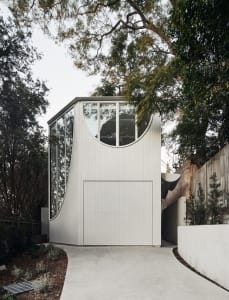 A minimalist, white exterior house extension constructed from concrete with large glass windows.
