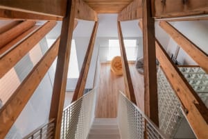 A modern interior space featuring wooden beams, a wooden staircase, and a floor-to-ceiling glass wall.