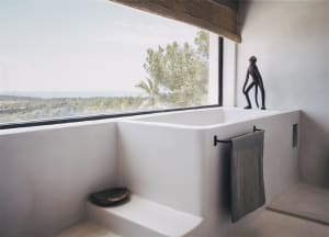 Modern minimalist bathroom featuring a concrete bathtub and towel rack with a view of the ocean through a large window.