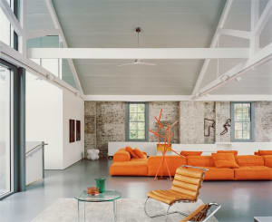 A spacious modern living room with exposed brick walls, orange sofas, and a minimalist design.