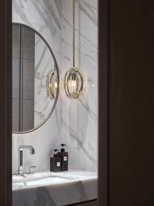 A sleek, modern bathroom with marble walls, a circular mirror, and a hanging crystal chandelier.