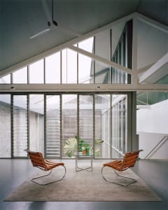 A minimalist living room with glass and metal furniture, large windows, and natural light.