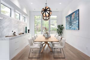 A modern dining room featuring white furniture and a marble backsplash with a geometric light fixture hanging above the table